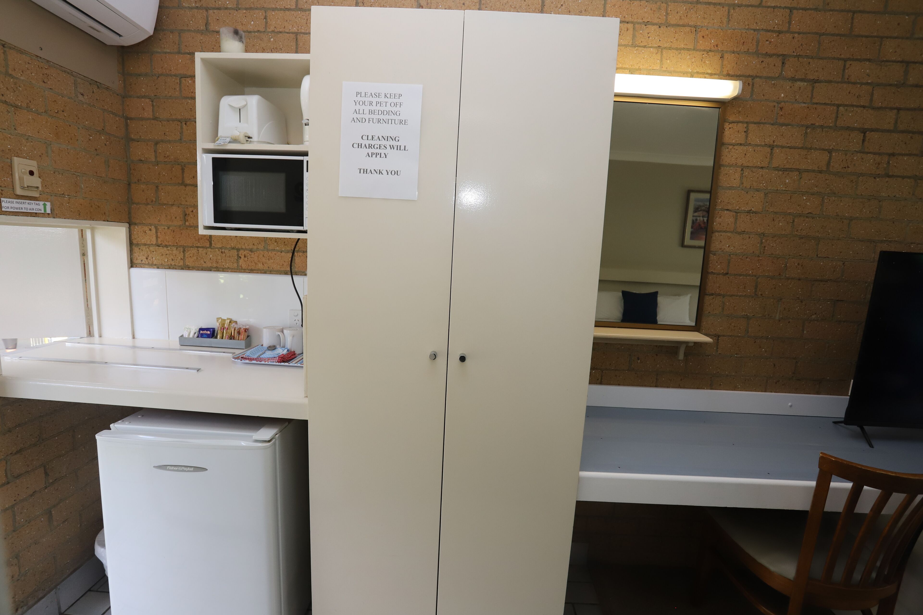 A kitchenette with a microwave, a refrigerator, and a sink. There is a sign on the refrigerator door.