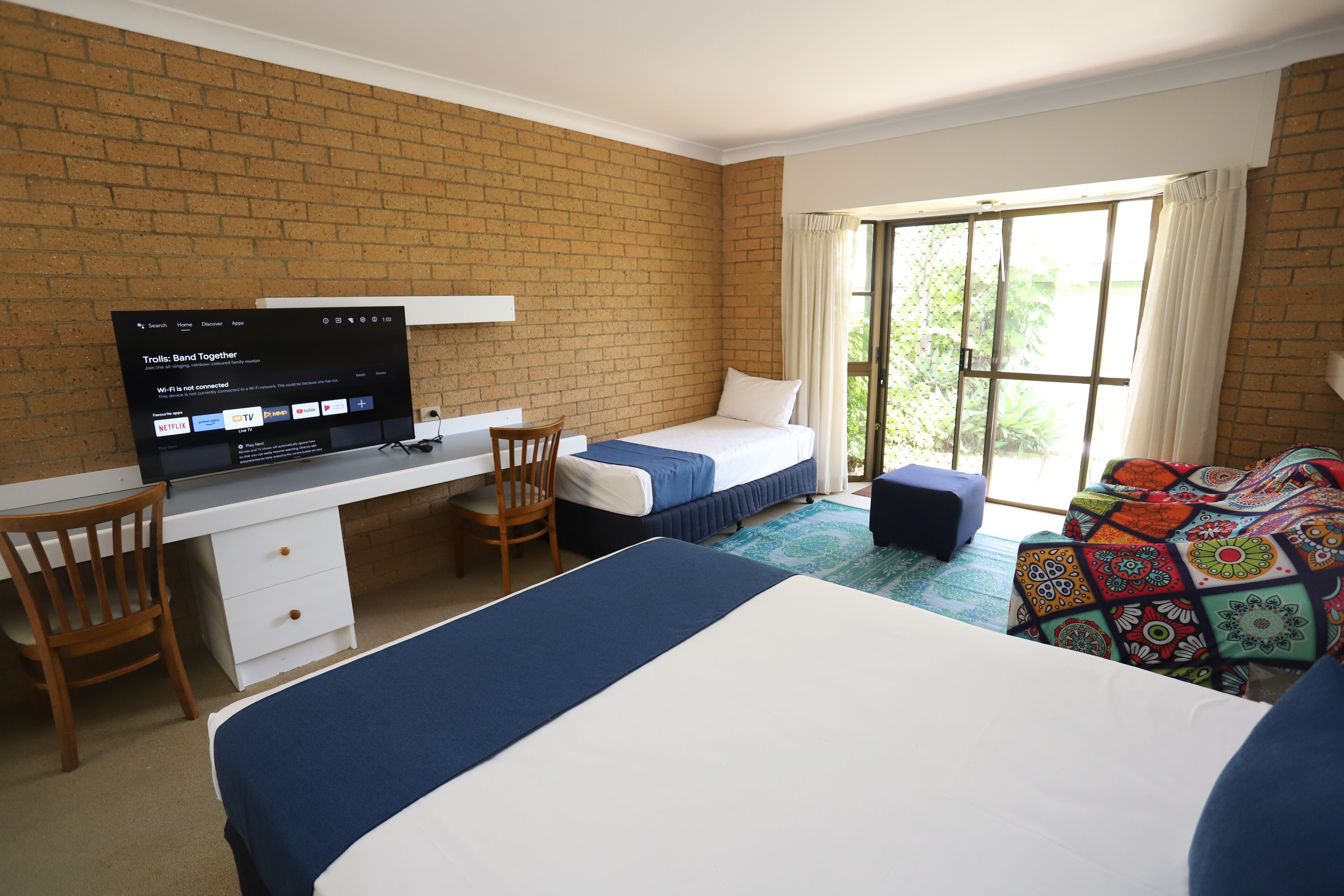 A room with a desk, two beds, a TV, and a window with curtains.