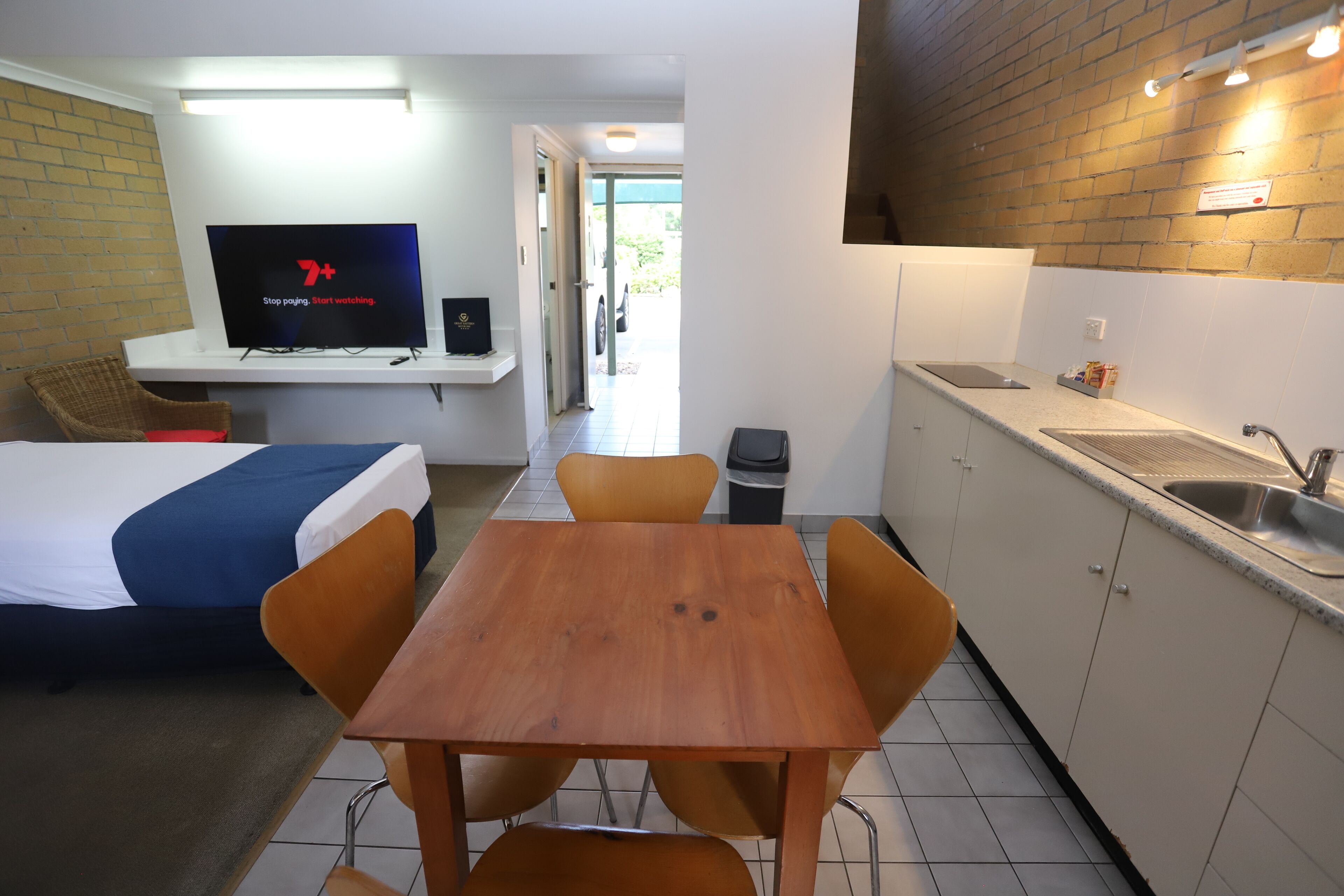 A compact hotel room with a bed, a TV, a small dining table, and a kitchenette.