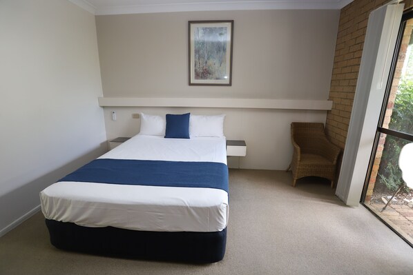 A bedroom with a bed, a chair, a window, and a painting on the wall.