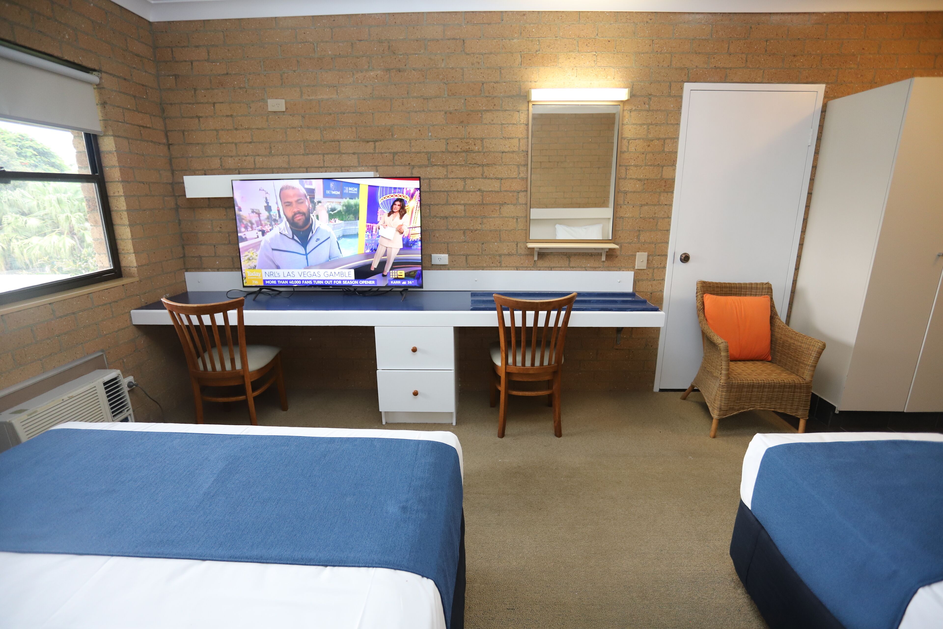 Ett hotellrum med två sängar, ett skrivbord med en tv, en stol och en garderob.