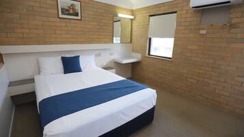 A hotel room with a bed, a small bedside table, a window with blinds, a wall-mounted air conditioner, and a picture on the wall.