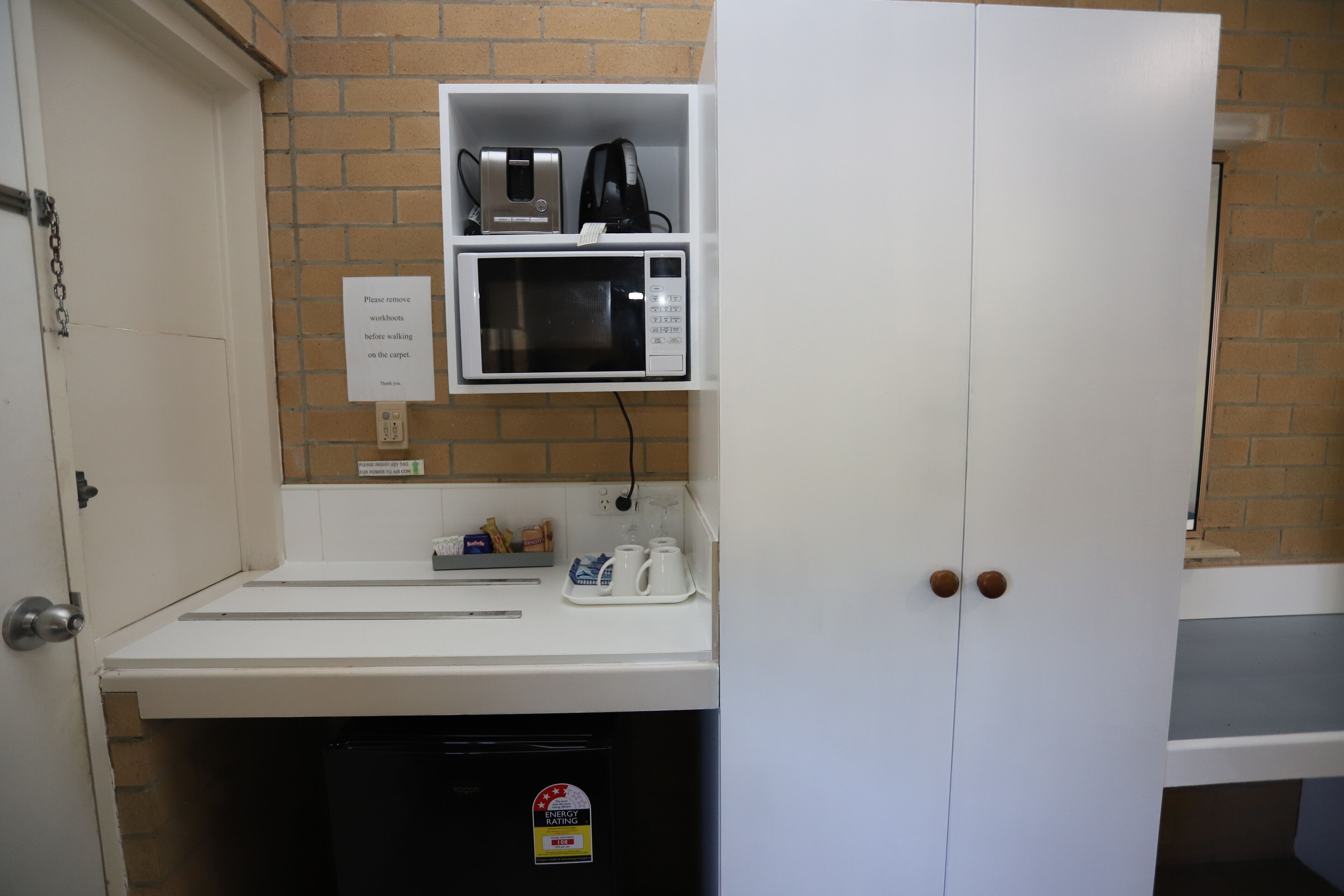A kitchen with a microwave, coffee maker, and a sign instructing to remove workbooks before walking on the carpet.