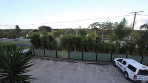 A parking area with a white utility vehicle, a green fence, and a row of palm trees.