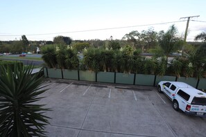 A parking area with a white utility vehicle, a green fence, and a row of palm trees.