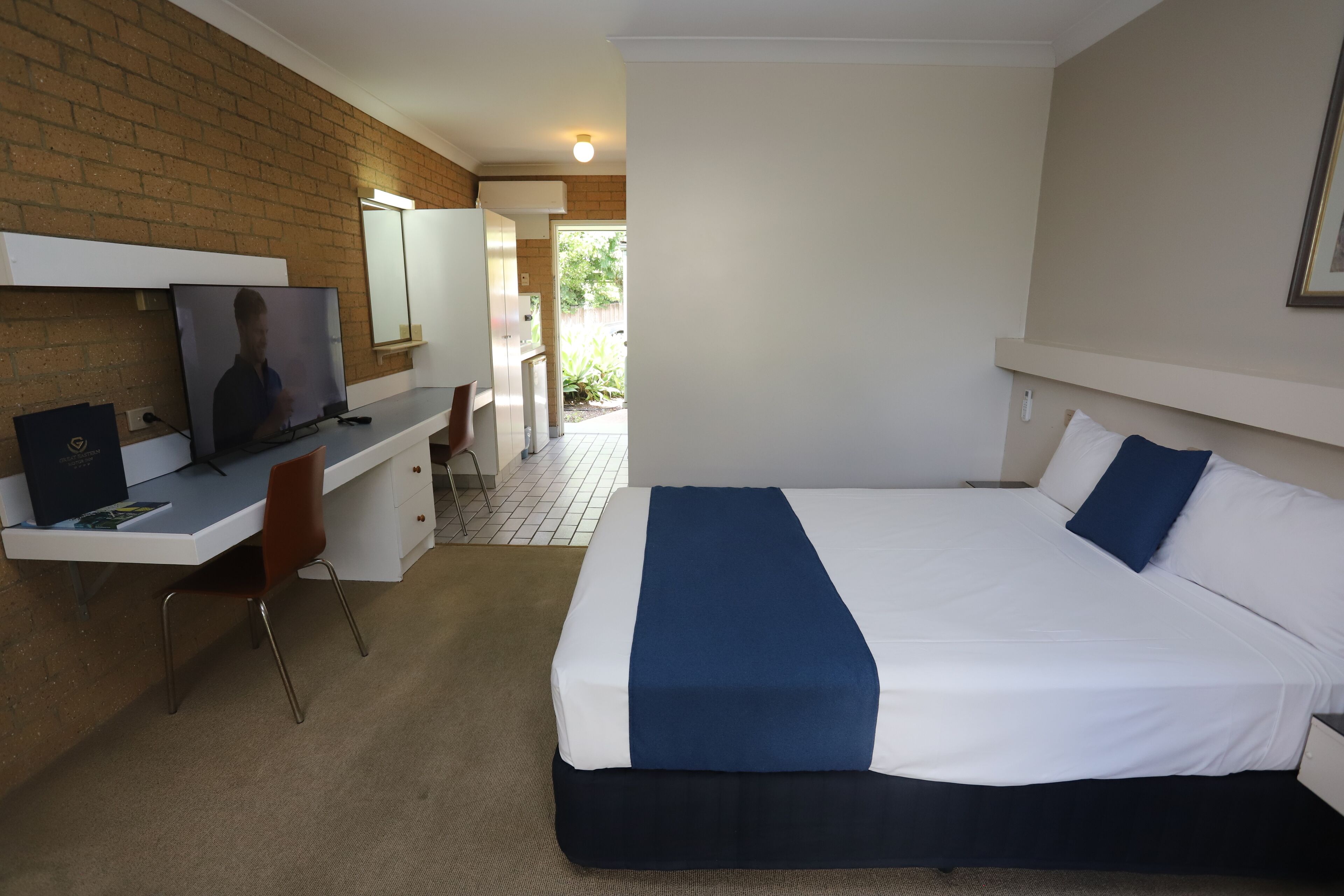 Een hotelkamer met een bed, een bureau met een televisie, een stoel en een badkamer zichtbaar door een geopende deur.