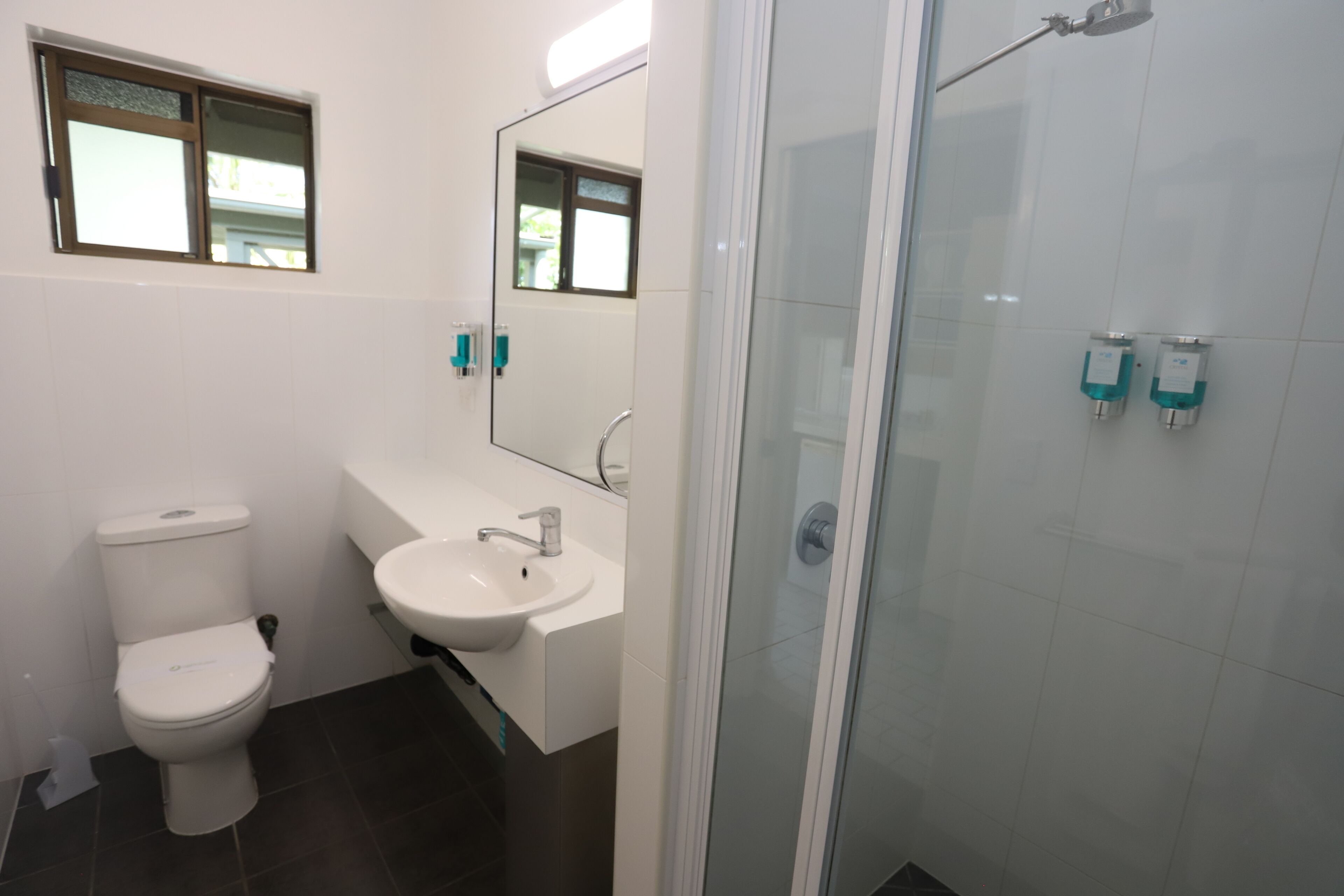A bathroom with a toilet, sink, mirror, and shower.