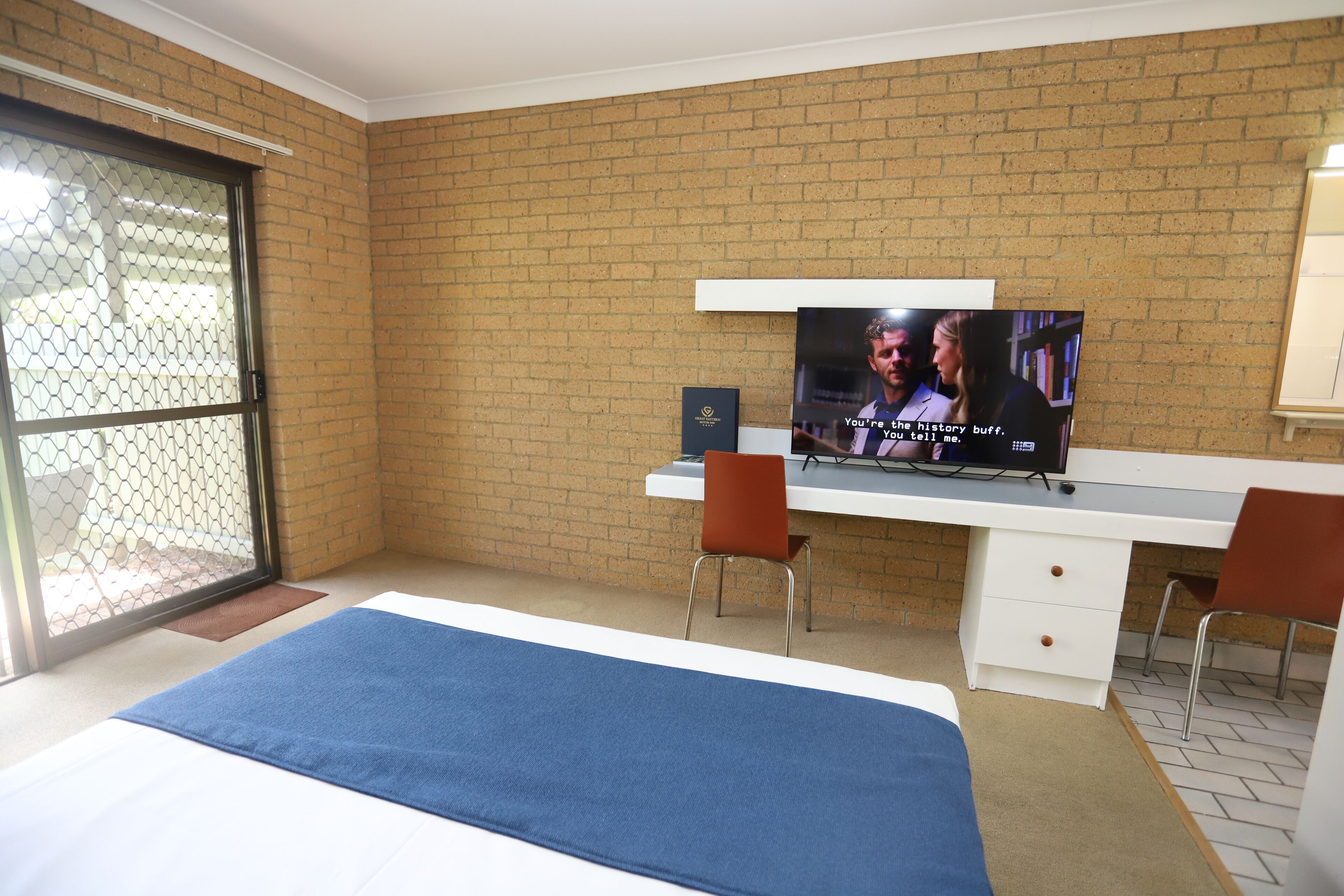 A hotel room with a bed, a desk with a computer, and a television.