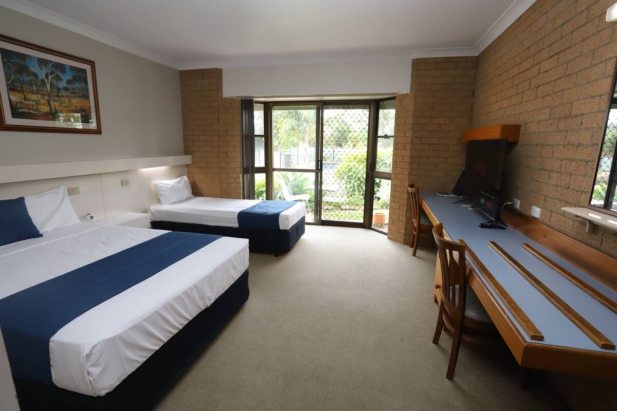 Quarto de hotel com duas camas, uma escrivaninha e uma janela grande.