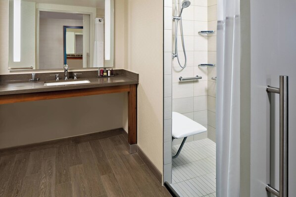 A modern bathroom with a wooden vanity, a large mirror, a shower area, and a glass-enclosed shower stall.