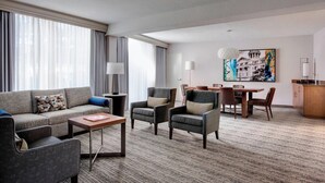 A hotel room with a sofa, armchairs, a coffee table, a dining table with chairs, and a painting on the wall. - Houston Airport Marriott at George Bush Intercontinental (Houston)