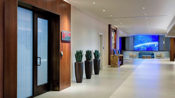 A modern hotel lobby with a reception desk, seating area, and a large screen displaying a space-themed image. - Houston Airport Marriott at George Bush Intercontinental (Houston)
