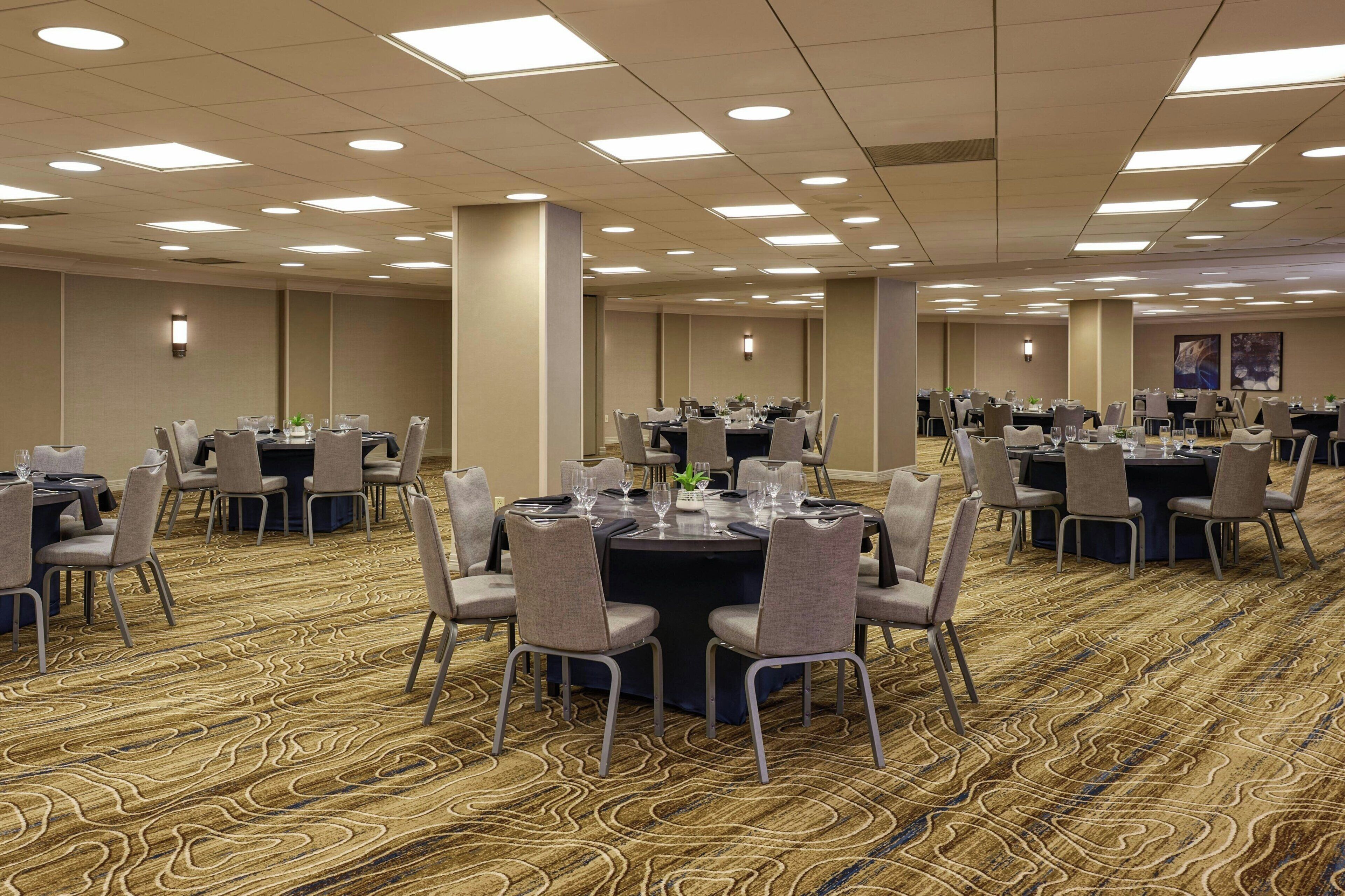 A conference room with round tables, chairs, and a carpeted floor.
