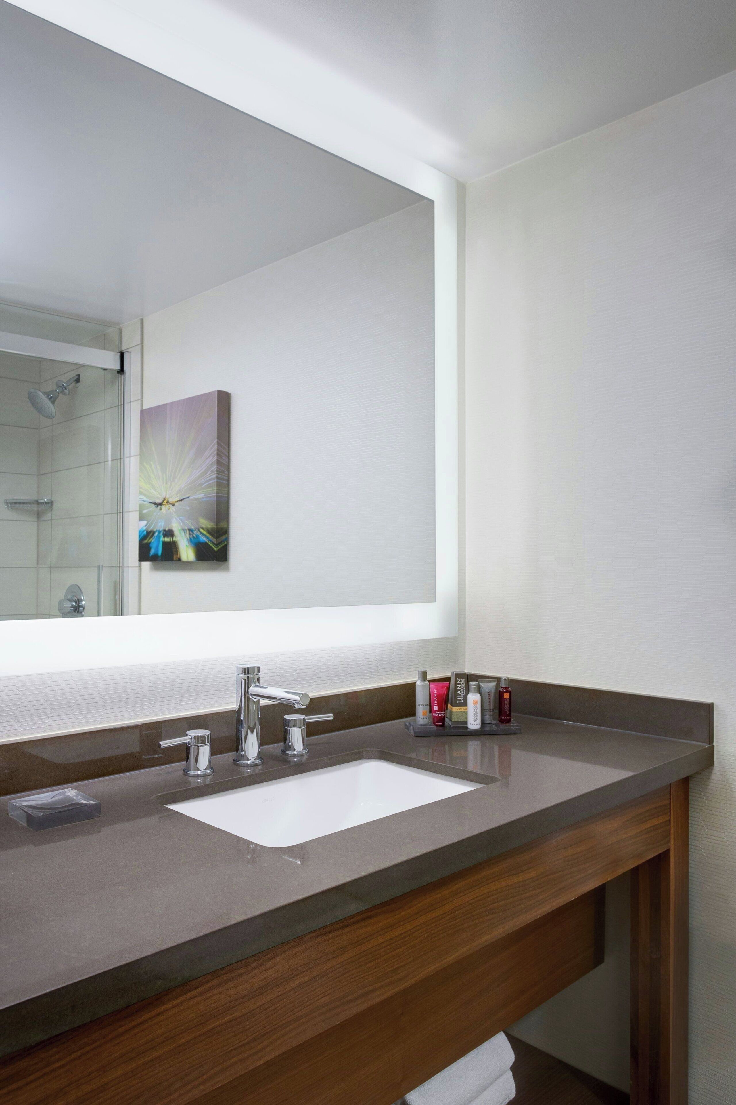 A modern bathroom with a large mirror, a double sink, and a wooden vanity.