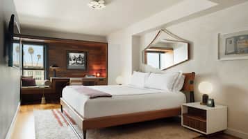 A modern bedroom with a large bed, bedside tables, a mirror, and a view of palm trees through the window.