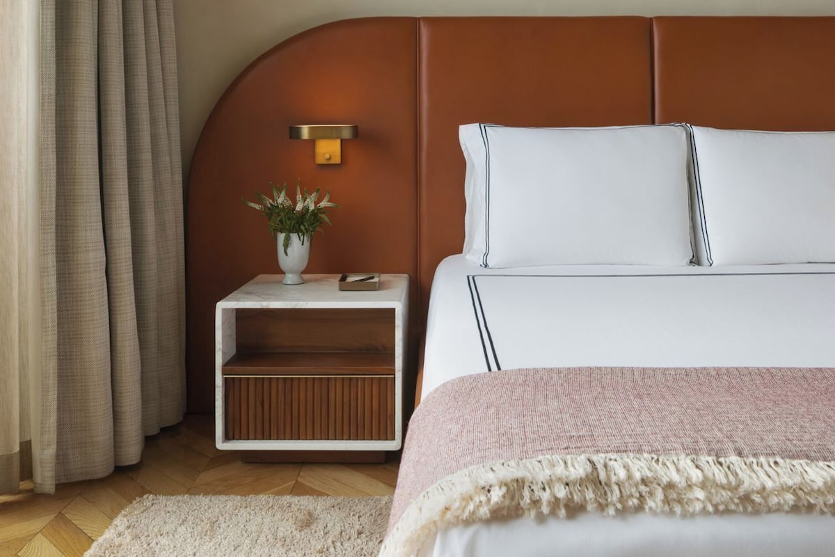 A bedroom with a bed, a nightstand, a lamp, a plant, and a window with curtains.