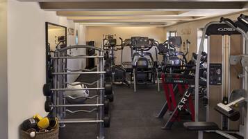 A gym with various exercise machines, a mirrored wall, and a basket with boxing gloves.