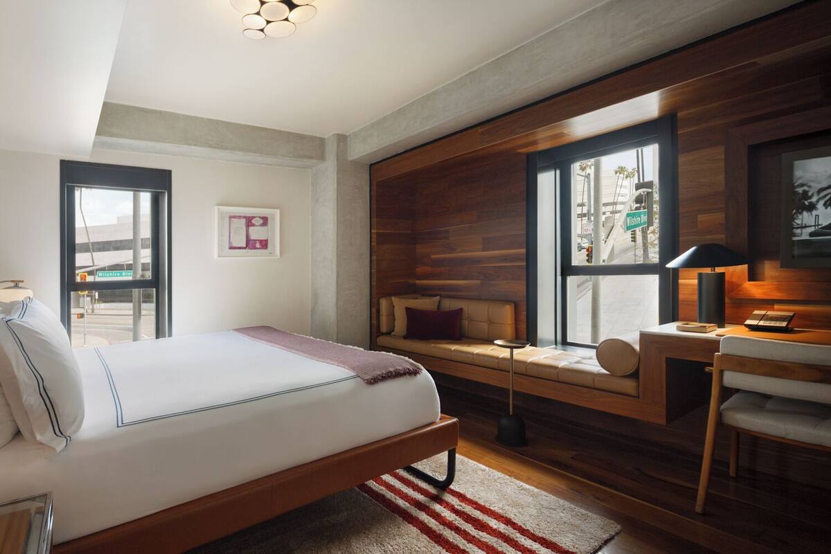 A modern hotel room with a bed, a seating area with a view, and a desk with a lamp.