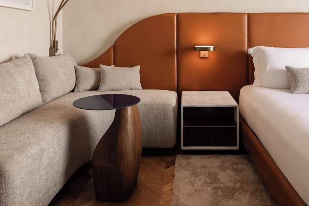 A modern hotel room with a curved headboard, a sofa, a bed, a small table, and a floor lamp.