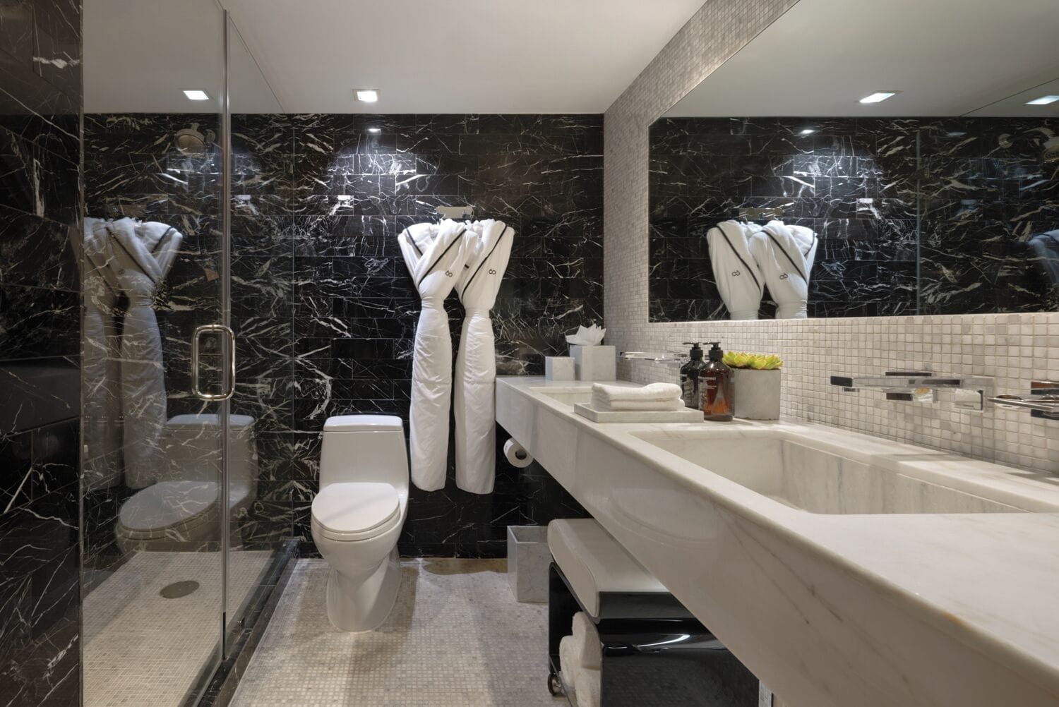 Een moderne badkamer met een douchecabine van glas, een wit toilet en een marmeren wastafelmeubel met een spiegel.