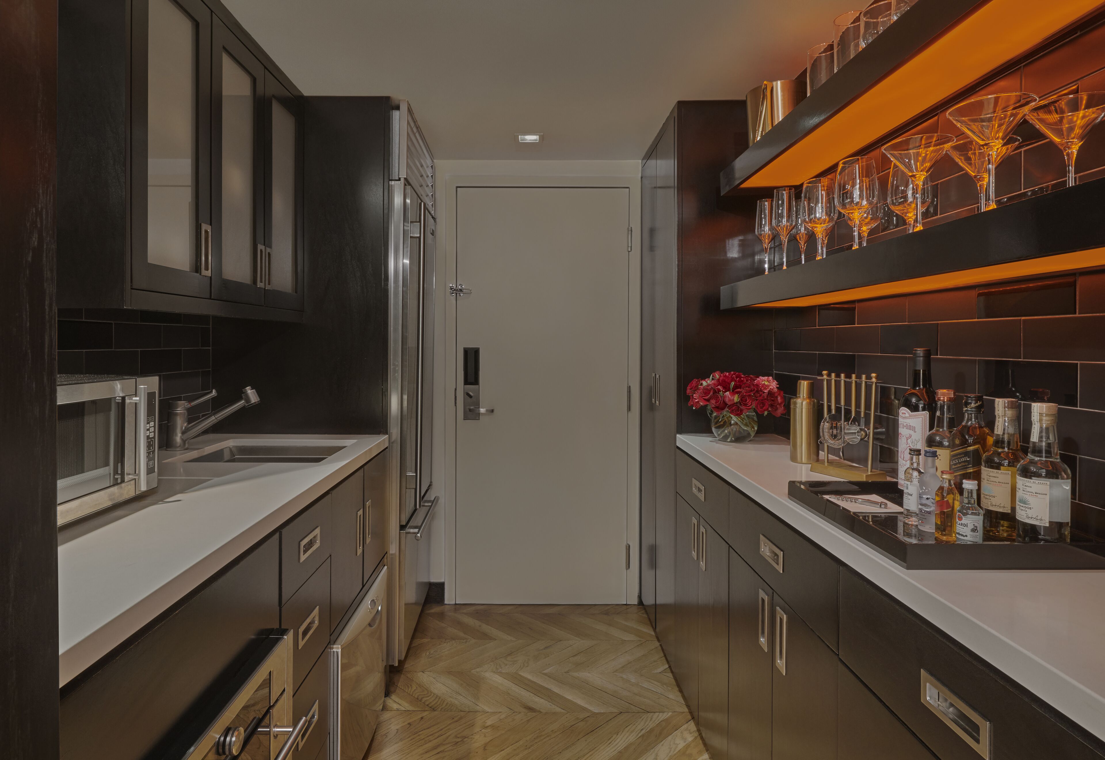 Una cocina moderna con armarios oscuros, un microondas, un lavamanos y una encimera con varias botellas y un florero.