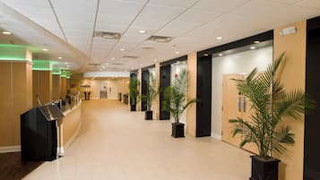 A hotel corridor with a reception desk, potted plants, and a modern ceiling design.