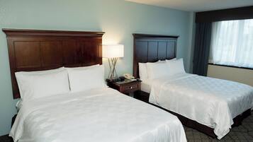 A hotel room with two beds, a nightstand with a lamp, and a window with curtains.
