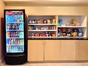 A vending machine with various drinks and snacks, a shelf with packaged goods, and wooden cabinets.