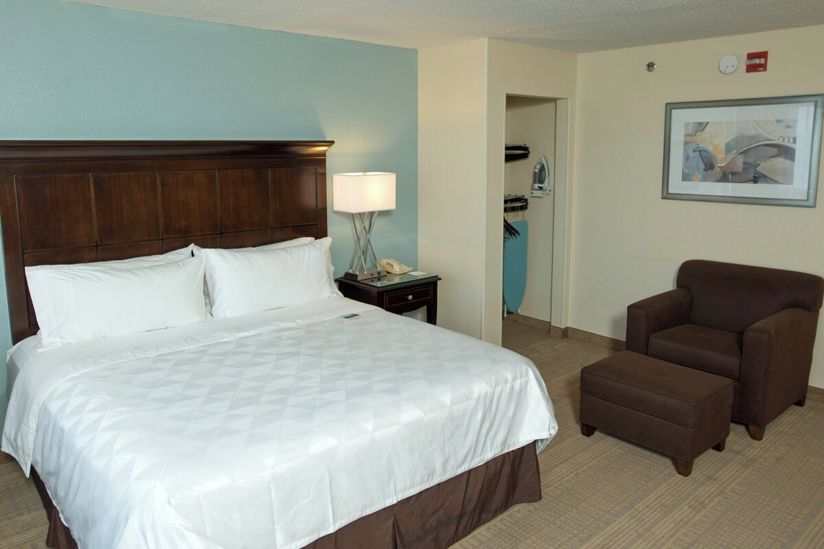 Una habitación de hotel con una cama grande, una silla, una mesita de noche y una lámpara.