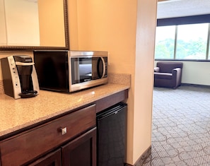 A kitchenette with a Keurig coffee maker, a microwave, a dishwasher, and a window with a view of trees.