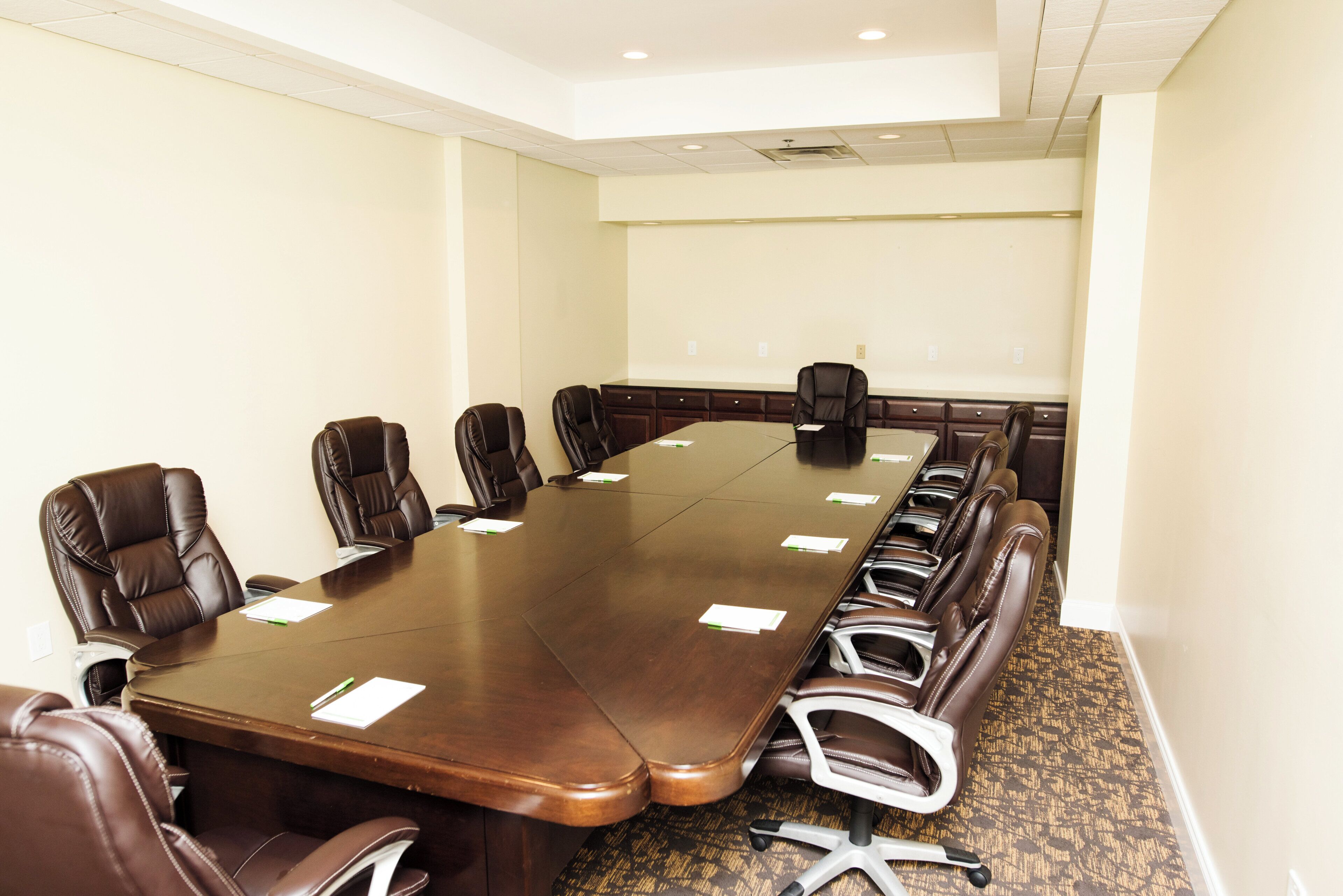 A conference room with a long table, multiple chairs, and a carpeted floor.