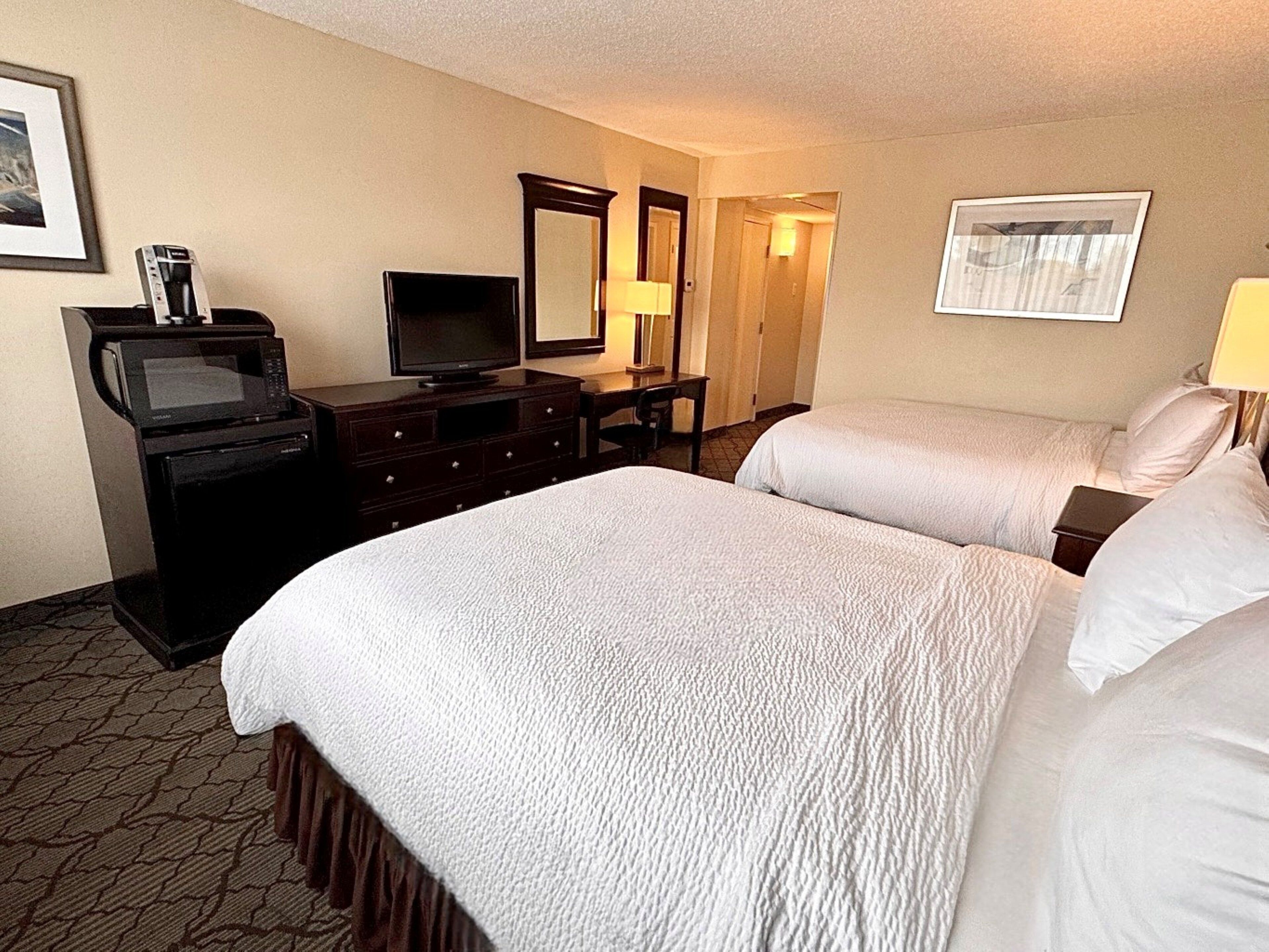 A hotel room with two beds, a TV, a microwave, a dresser, and a mirror.