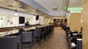 A bar area with a long counter, multiple bar stools, and a television screen. - Holiday Inn Birmingham-Airport by IHG (Birmingham)