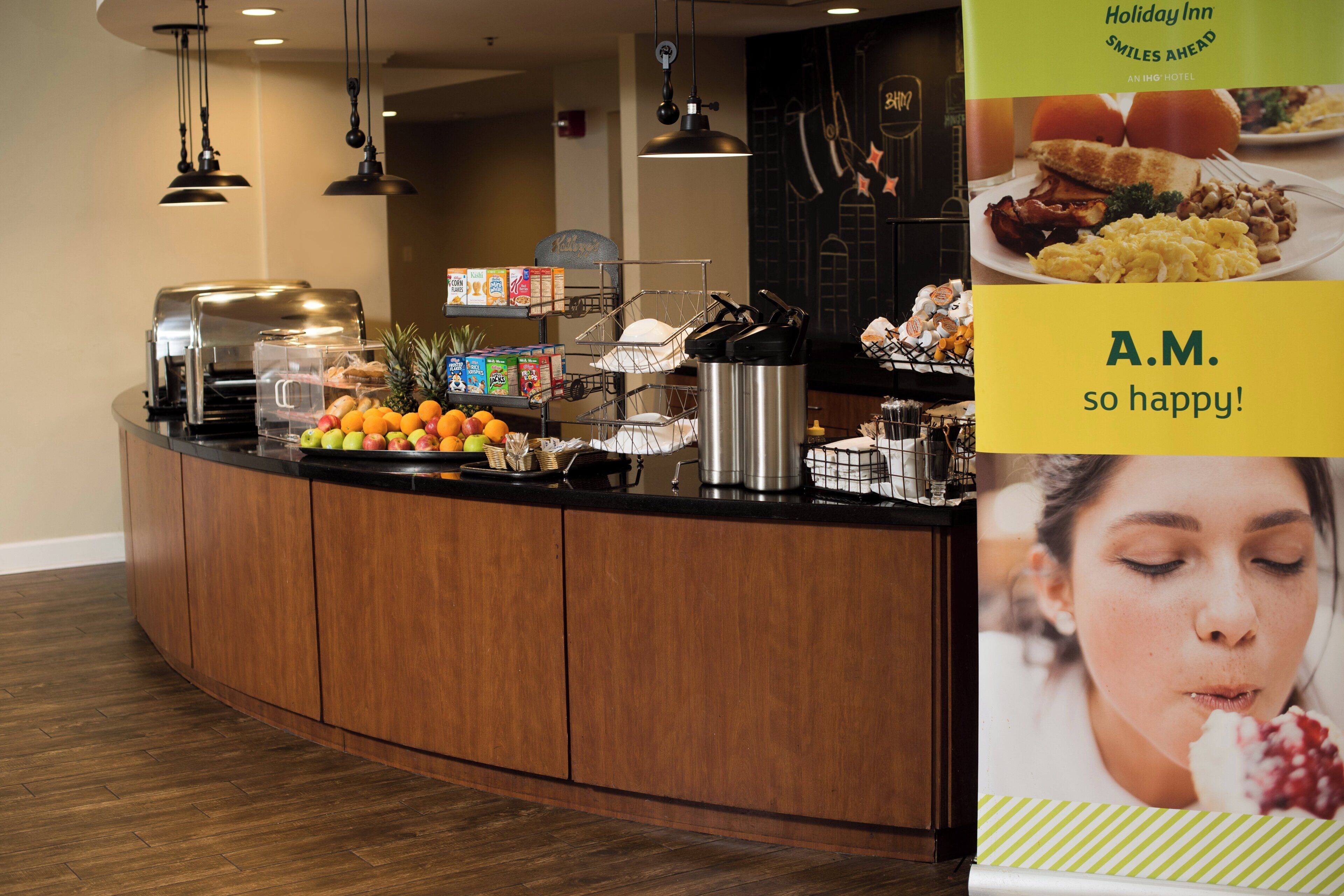 A breakfast buffet area with various food items, a coffee machine, and a fruit display.