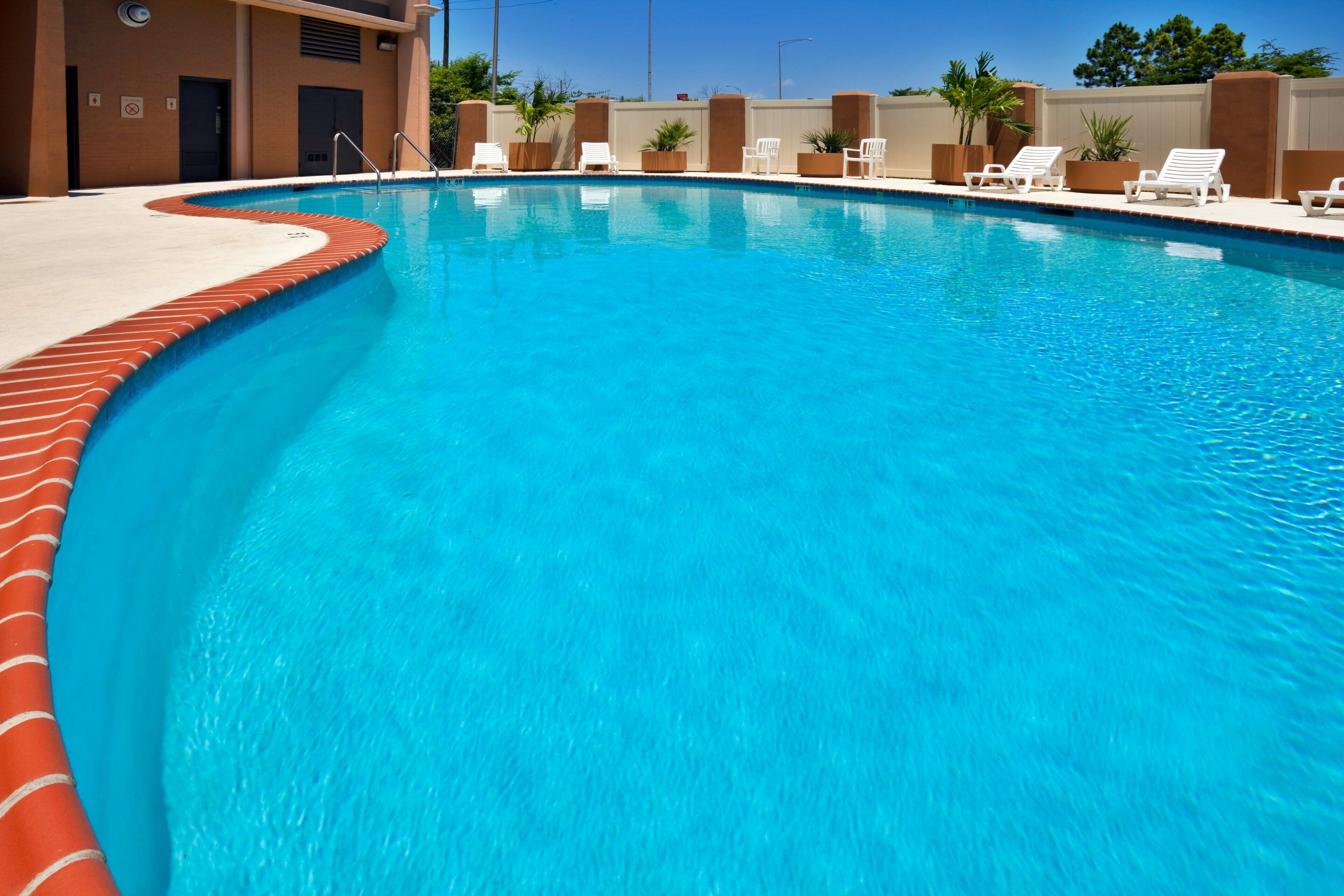 A swimming pool with a curved edge, surrounded by lounge chairs and potted plants.