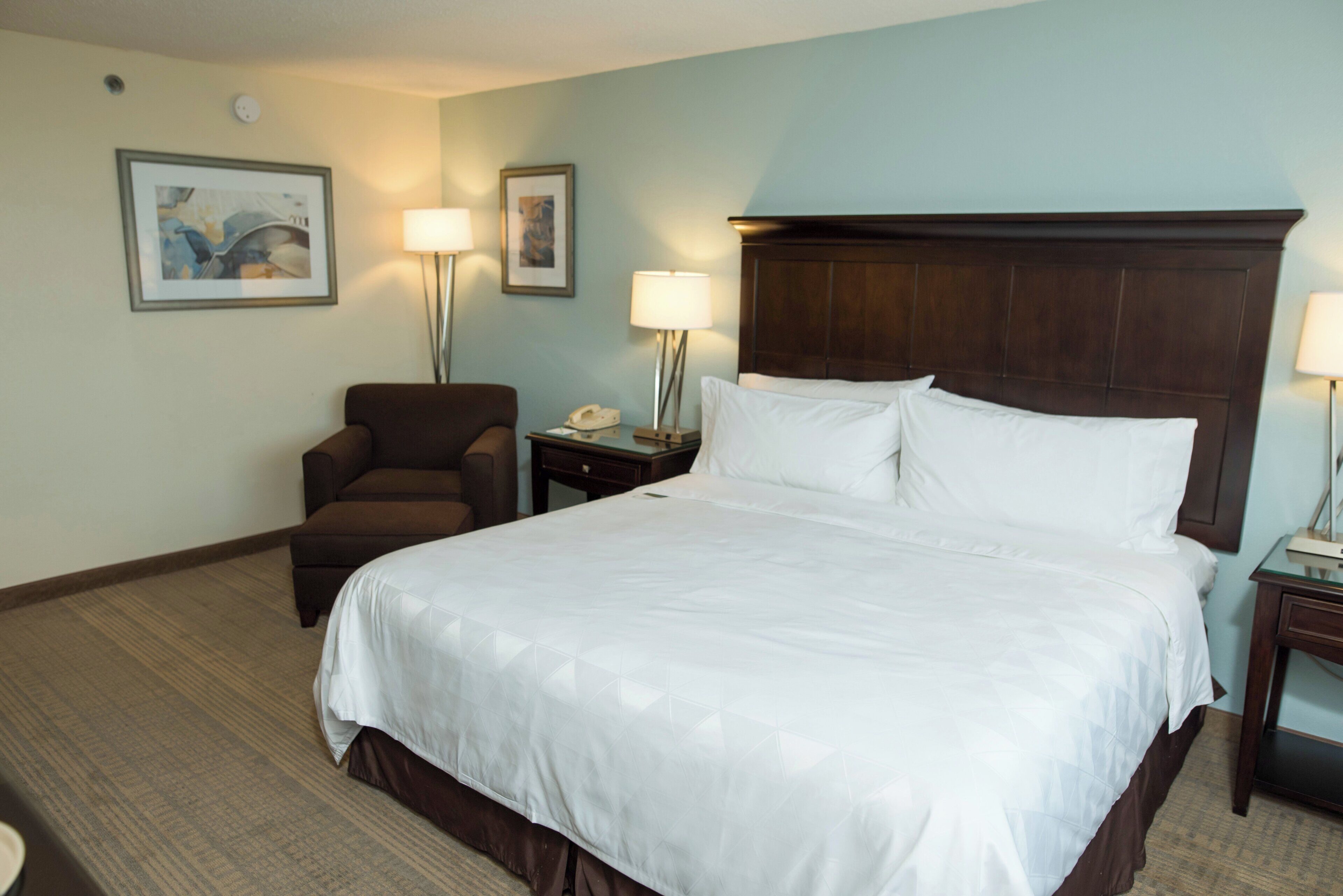 Habitación de hotel con una cama grande, una silla, una mesita de noche y dos lámparas de pared.