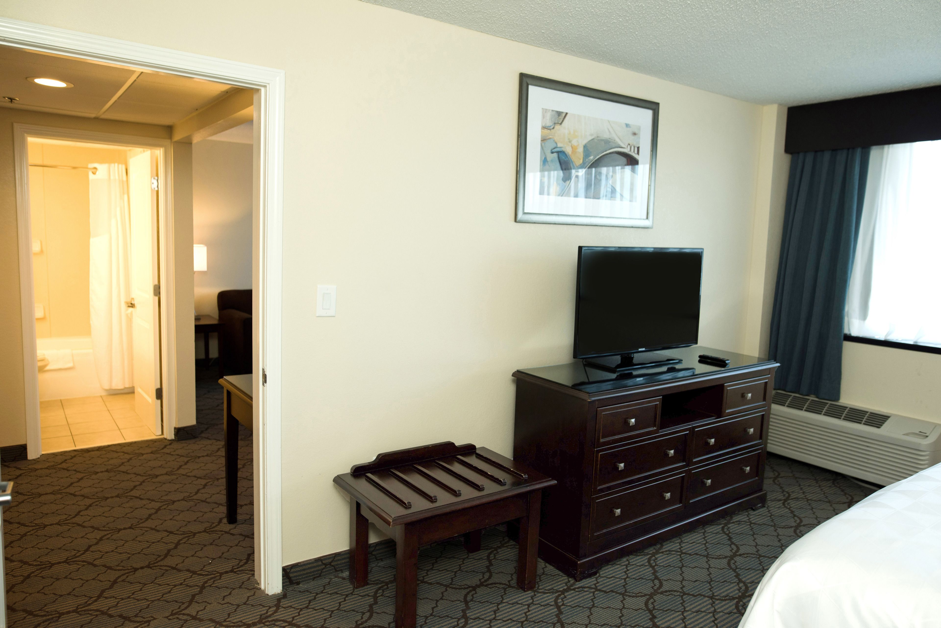 A hotel room with a bed, a dresser, a television, a small table, and a picture on the wall.