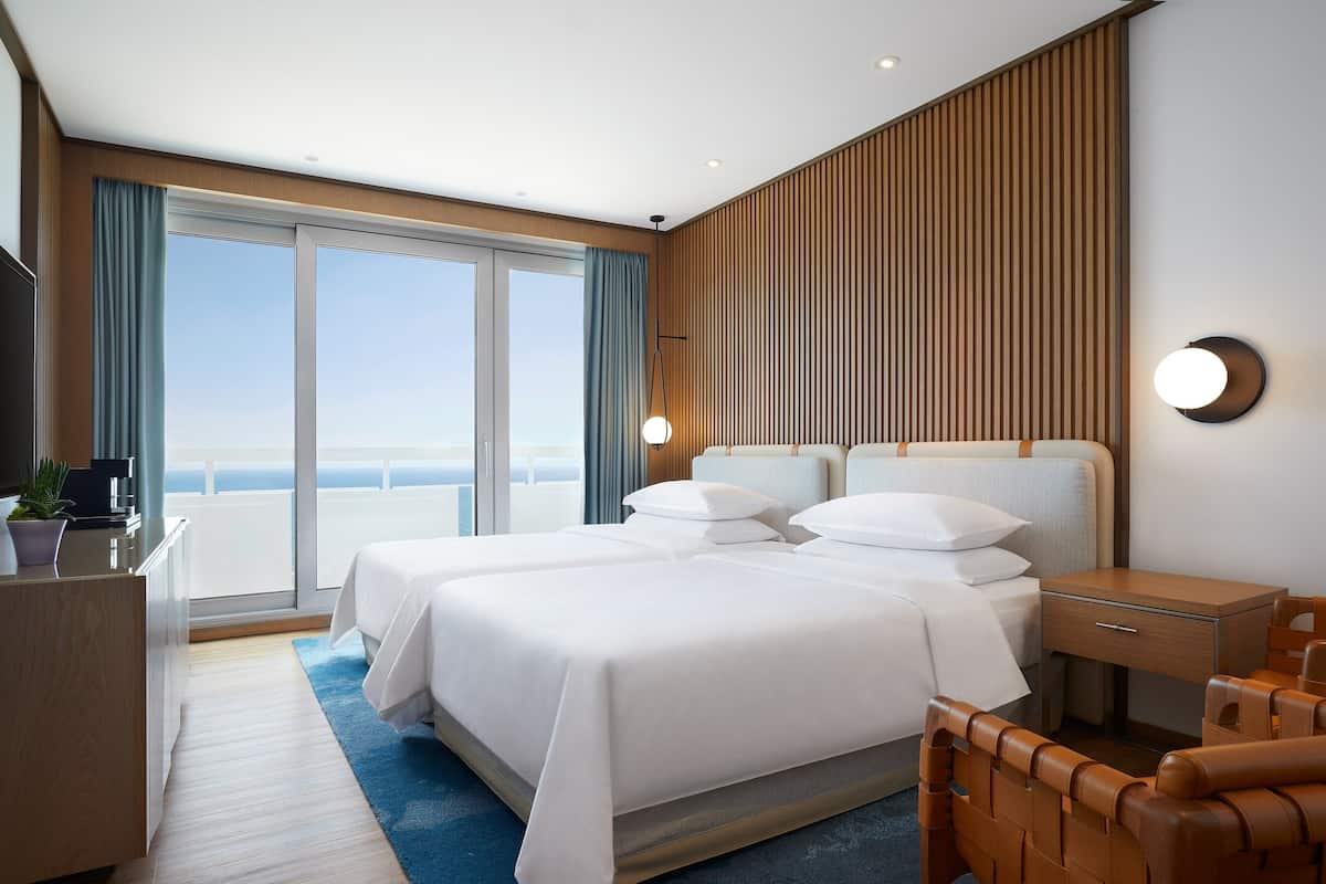 Habitación de hotel moderna con una cama grande, un escritorio, una silla y vistas al océano.