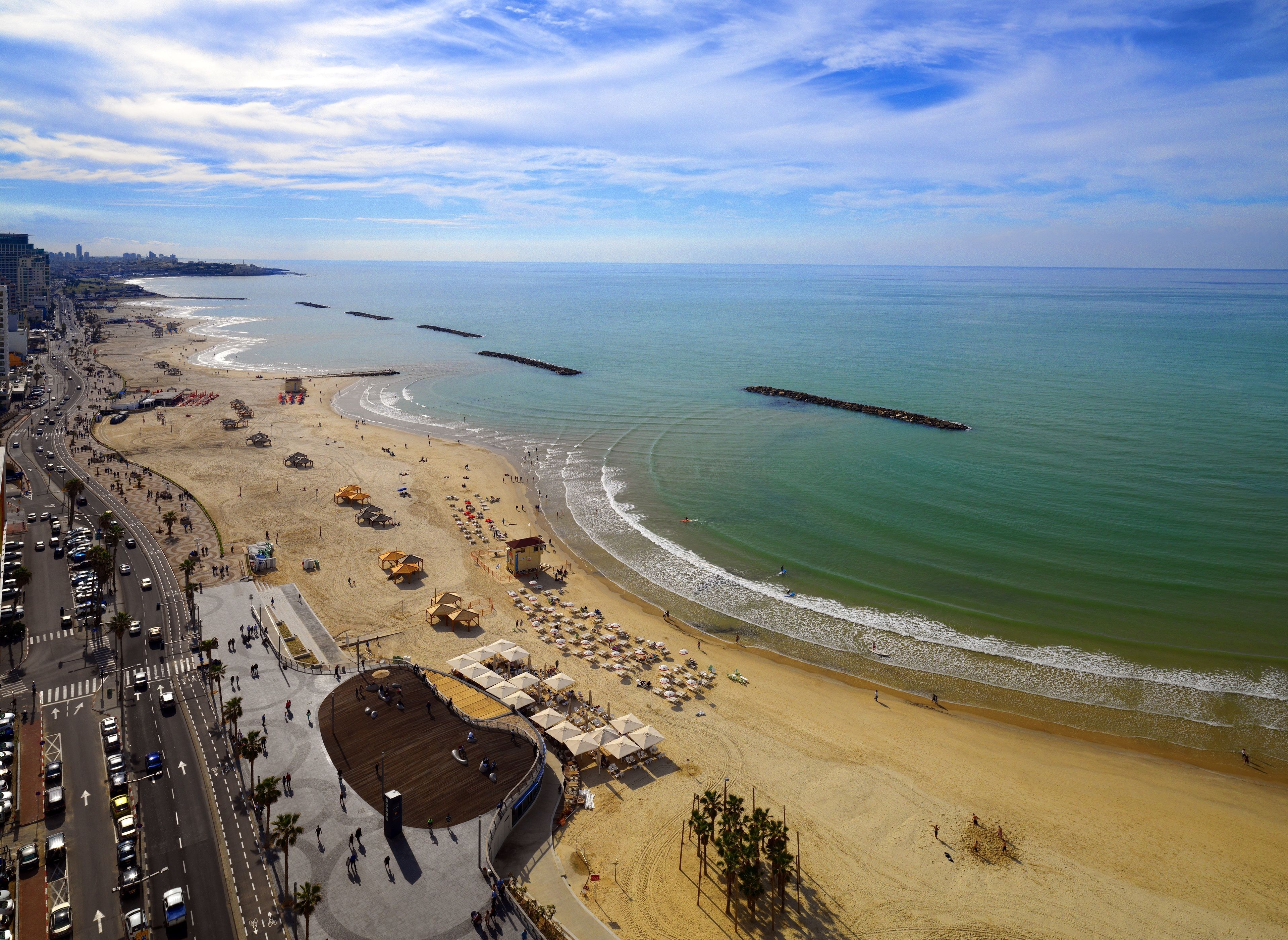 A coastal cityscape with a beach, promenade, and a boardwalk with umbrellas.