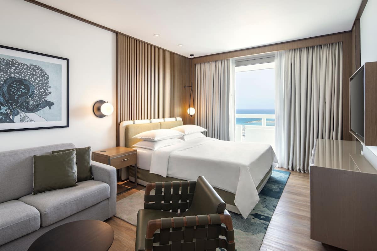 Una habitación de hotel moderna con una cama, un sofá, una silla, un escritorio y un televisor.
