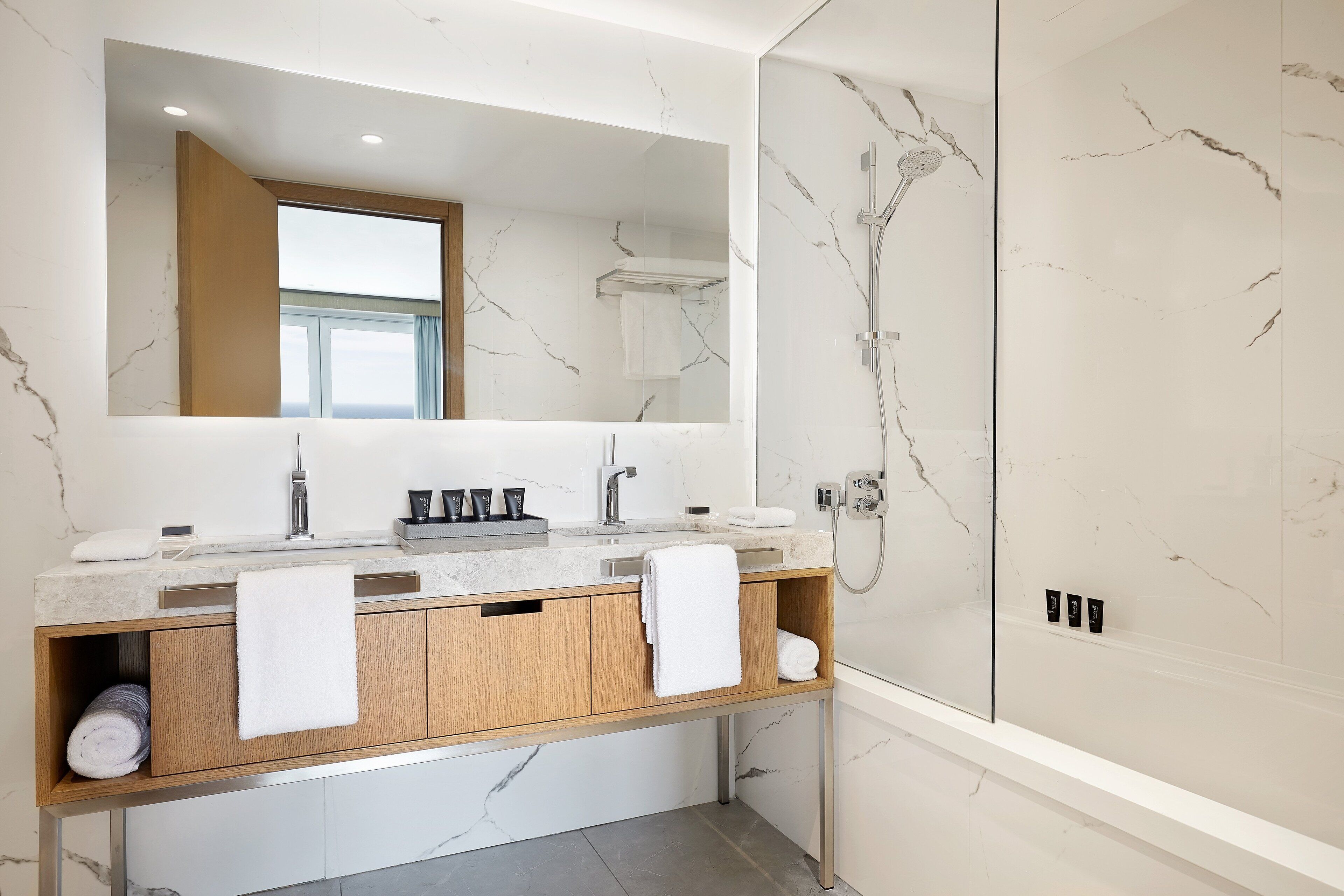 Une salle de bain moderne avec un meuble-lavabo en marbre, deux vasques et une douche à parois de verre.