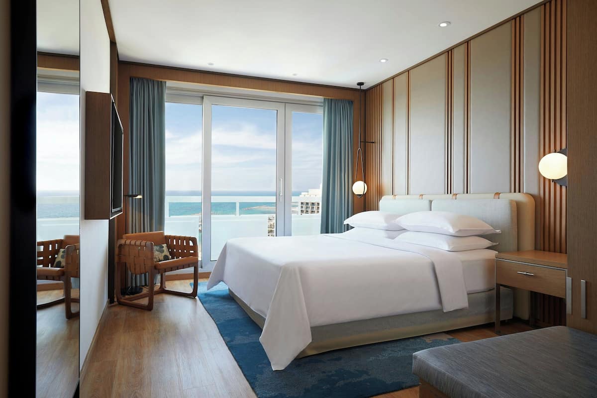 Habitación de hotel moderna con una cama grande, zona de estar con vistas y pared de paneles de madera.