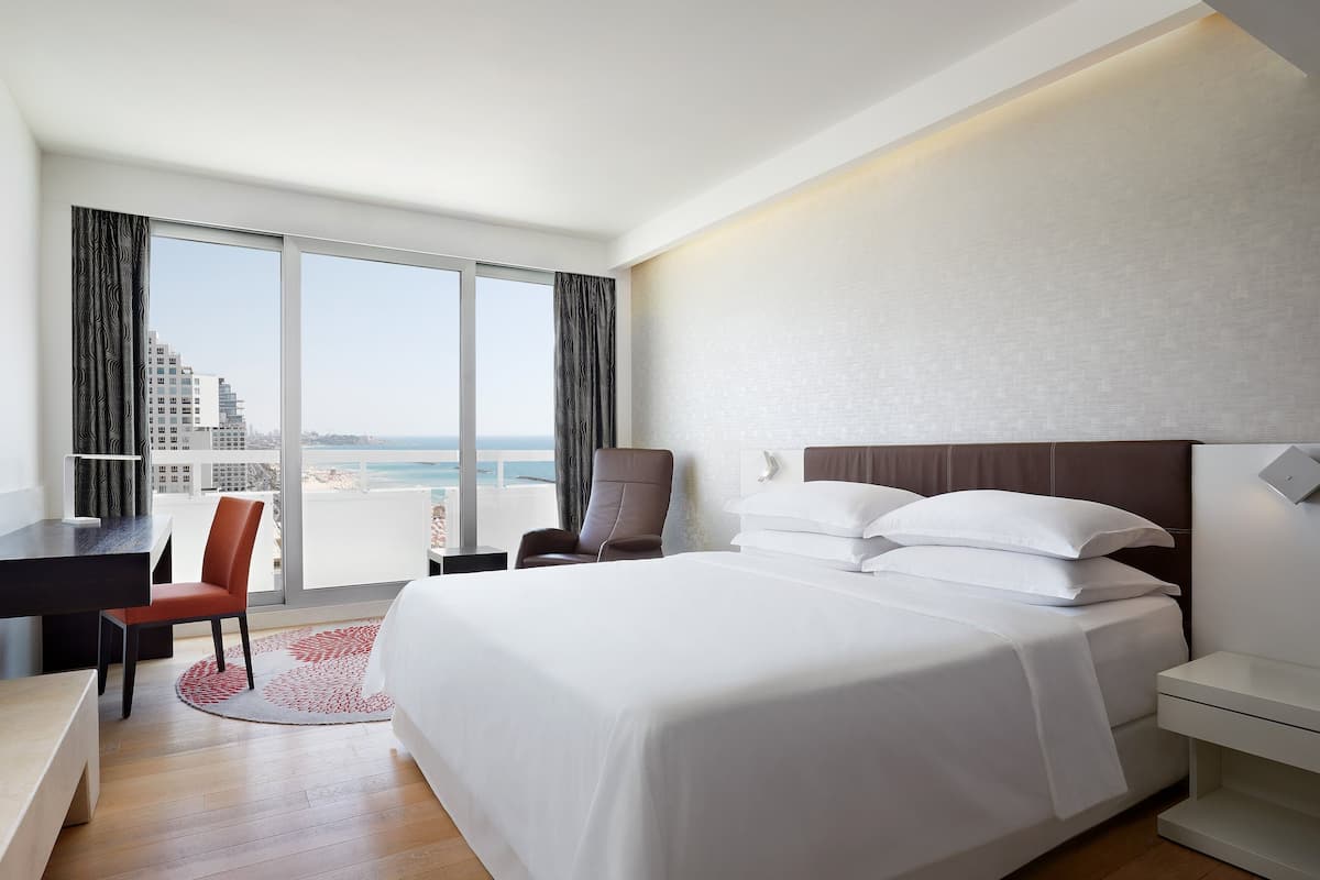 Habitación de hotel con una cama grande, un escritorio, una silla y vistas a la ciudad y al océano.