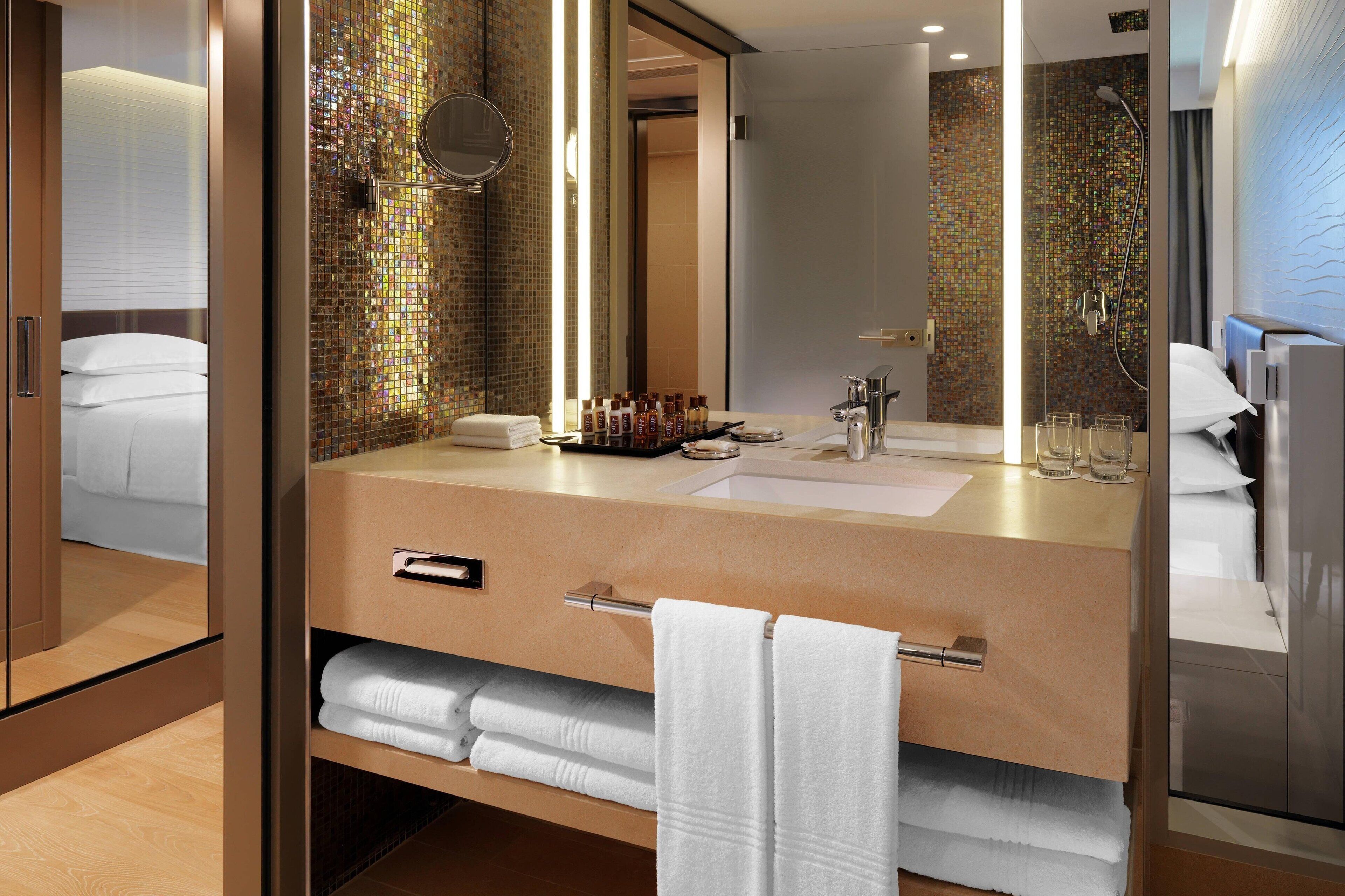 A modern bathroom with a large mirror, a shower, and a vanity with toiletries.