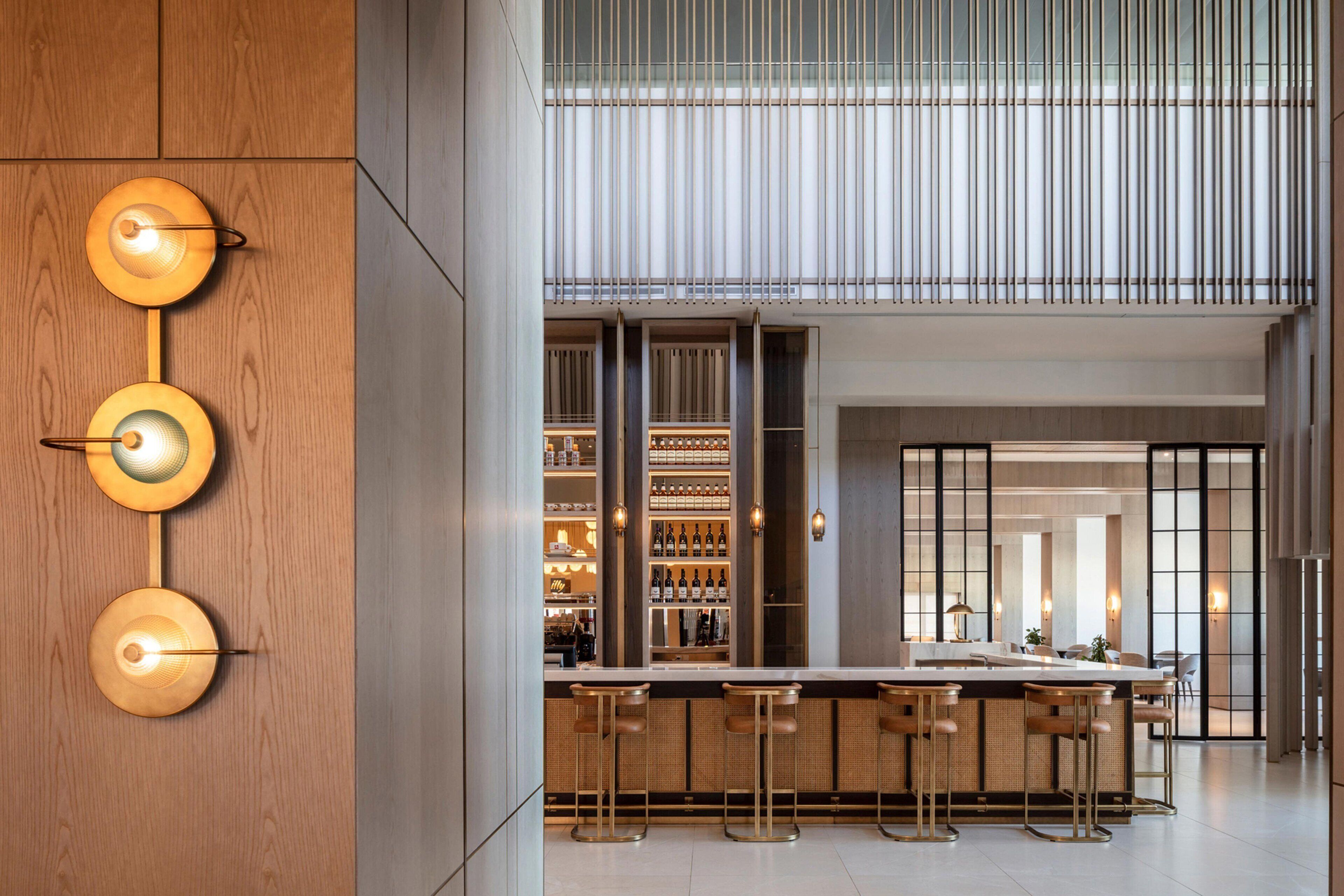 Zona bar moderna con soffitto alto, elementi in legno e bancone bar con sgabelli.