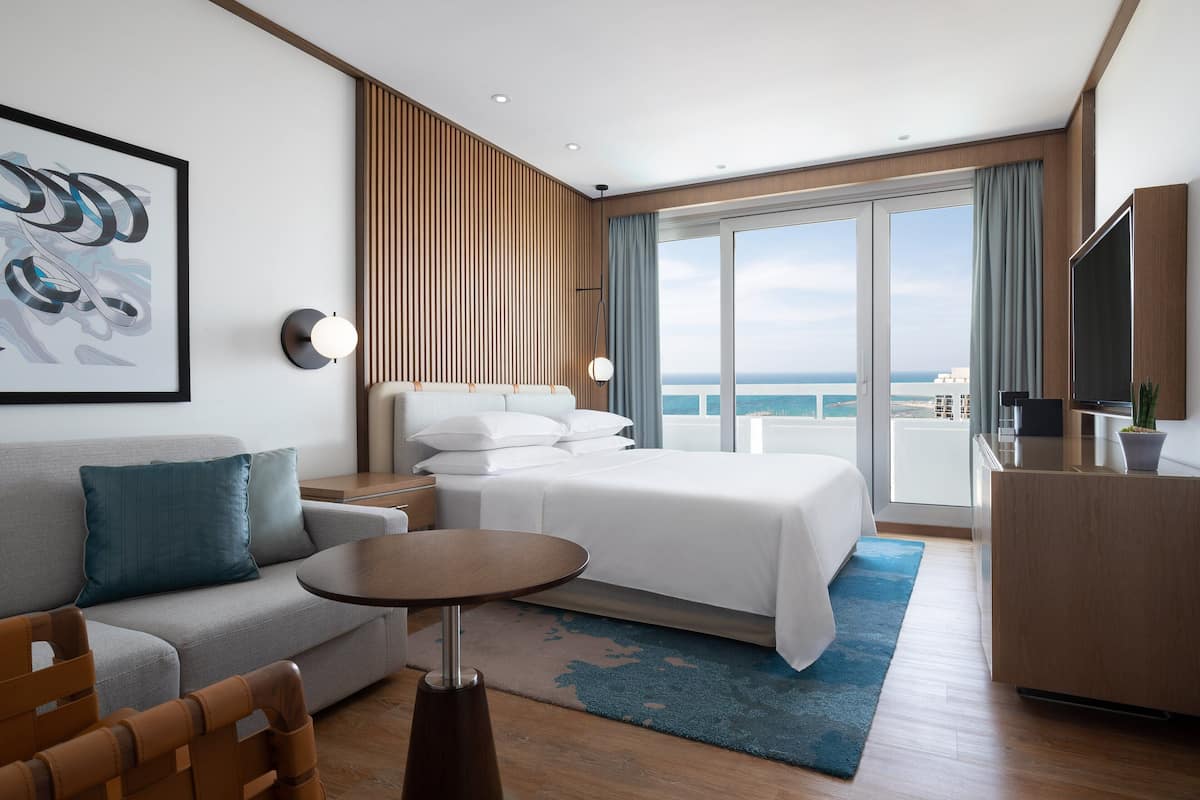 Una habitación de hotel moderna con cama, sofá, una mesita y televisor.
