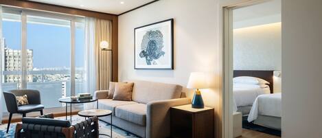 Una habitación de hotel moderna con un ventanal grande, un sofá, una silla, una mesita de noche con lámpara y una cama.