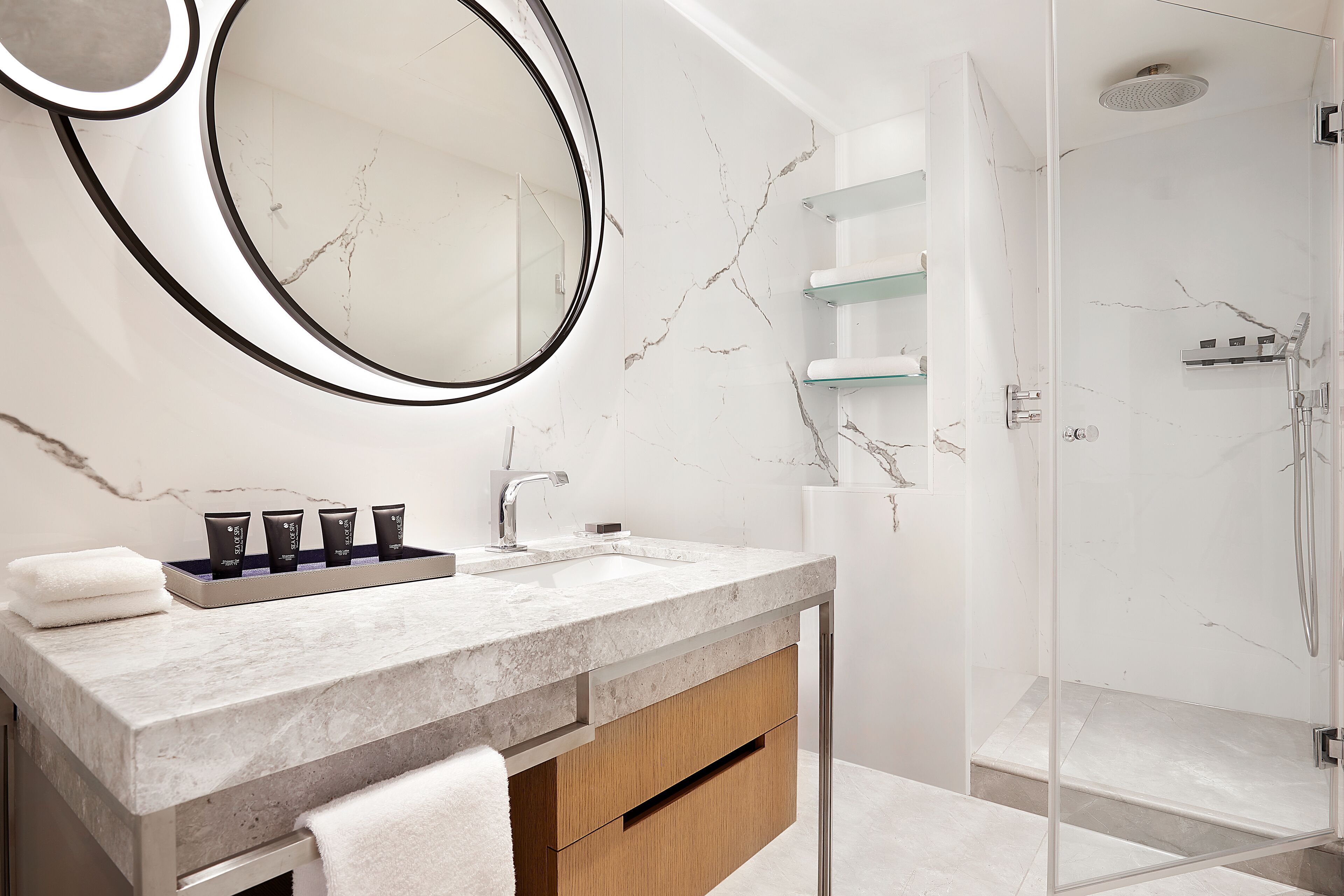 A modern bathroom with a marble countertop, a large mirror, and a glass-enclosed shower.