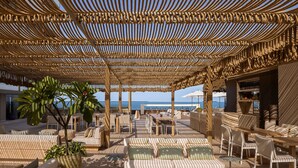A sunlit outdoor lounge area with wicker furniture, a large potted plant, and a view of the sea. - Sheraton Grand Tel Aviv (Tel Aviv)