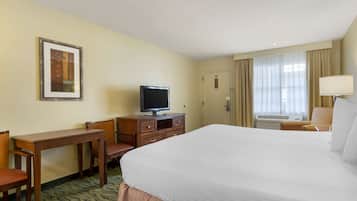 Una habitación de hotel con una cama grande, un escritorio con silla, televisión y ventana con cortinas.